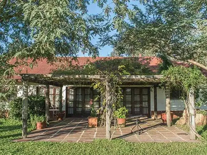 Rustic Patagonian lodge with pergola-covered patio, terracotta pots, and mature trees at Rincón del Socorro.