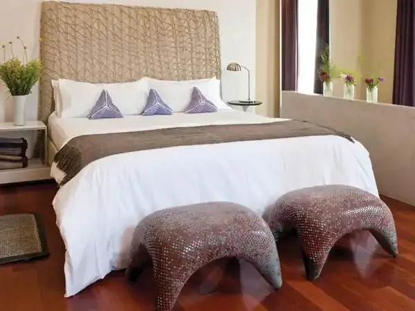 Luxurious hotel bedroom with woven headboard, white bedding, purple accents, and wooden flooring in a modern South American resort.