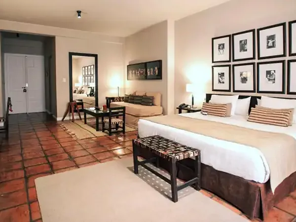 Spacious luxury hotel suite with two beds, terracotta tile floors, and black-framed artwork at Legado Mítico Buenos Aires.