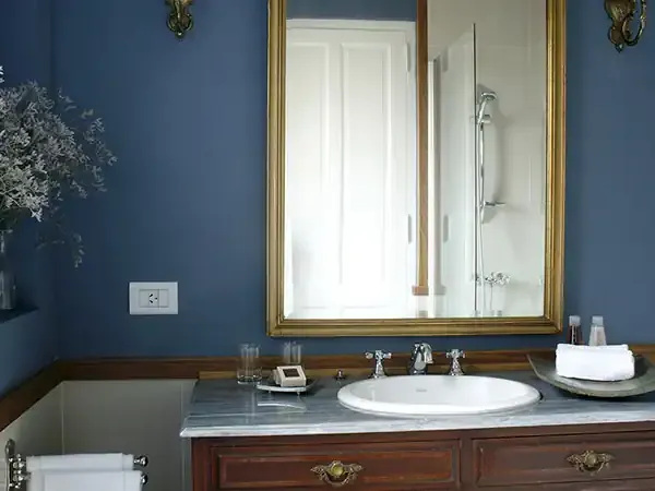 Elegant bathroom with deep blue walls, marble countertop, and gold-framed mirror reflecting luxury accommodation in Patagonia.