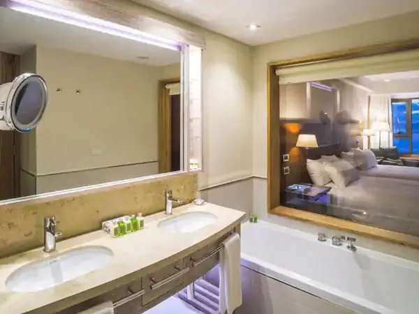 Luxury bathroom with dual vanities, illuminated mirror, and ocean views at Arakur hotel in Ushuaia.