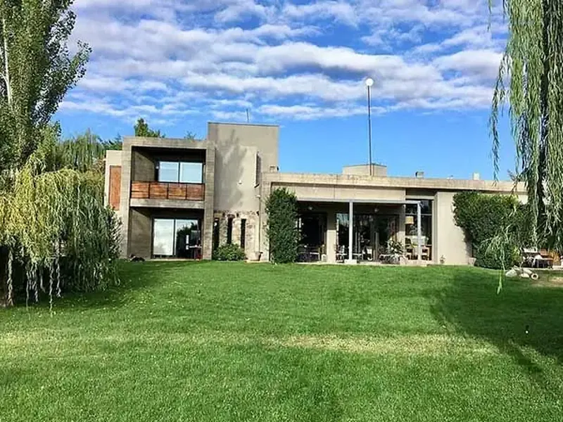 Modern architecture home at Finca La Azul with manicured lawn, weeping willows, and Patagonian landscape under blue sky.
