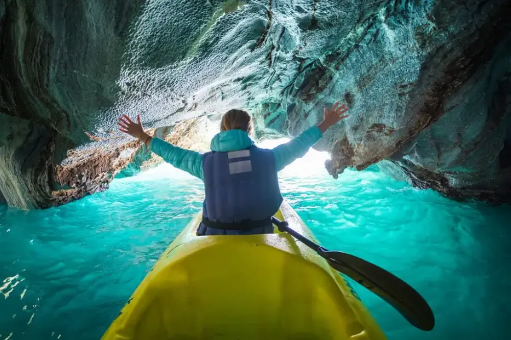 Kayaker paddling through turquoise waters beneath towering marble cave formations in Patagonia's Carretera Austral.