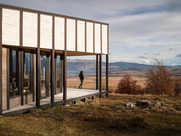 Modern lodge with expansive windows overlooks vast Patagonian steppe, mountains, and sky in Chilean Patagonia.