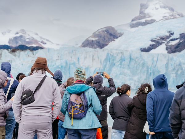 Tourists admire the massive blue ice formations of Perito Moreno Glacier in Patagonia while photographing the stunning mountain landscape.