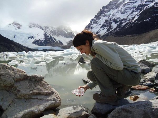 Woman collecting glacial ice at Laguna Torre with snow-capped peaks and icebergs in Patagonia.