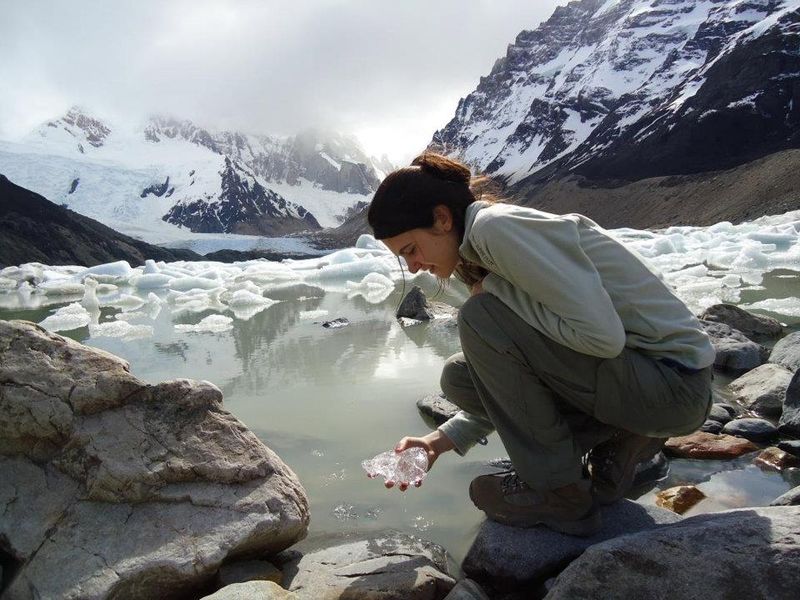 Woman collecting glacial ice at Laguna Torre with snow-capped peaks and icebergs in Patagonia.