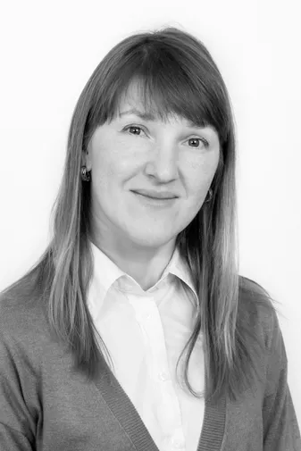 Black and white portrait of a woman with straight hair, wearing a white blouse and a cardigan, smiling softly against a plain background.