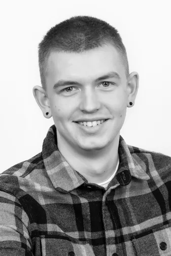Young man smiling, wearing a plaid shirt and earrings. Black and white portrait with a plain white background.