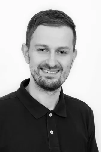 Smiling man with short hair and beard, wearing a dark polo shirt, against a plain background. Black and white photo.