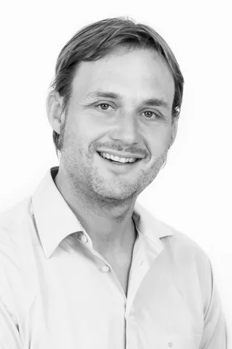 Smiling man with short hair, wearing a light-colored shirt, against a plain white background. Black and white image.