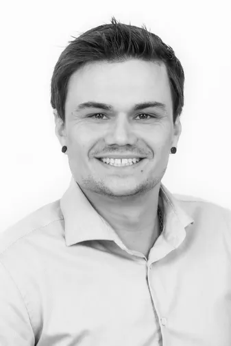 Smiling person with short hair and earrings in a button-up shirt, black and white portrait.
