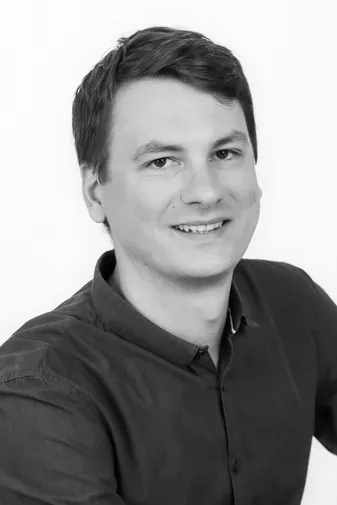 Smiling person with short hair wearing a dark shirt, positioned against a plain white background.