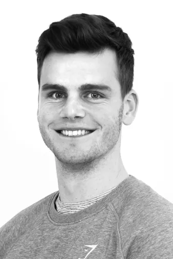 Smiling man in a gray sweater, with short dark hair, poses in a black-and-white portrait against a white background.