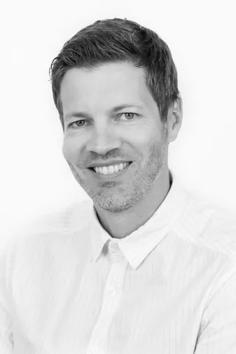 Smiling man with short hair and a beard, wearing a white button-up shirt, in a black and white portrait.