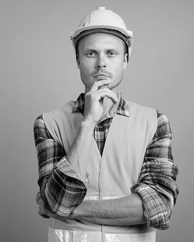 Man in a hard hat and safety vest, with a thoughtful expression, resting his chin on his hand. Black and white image.