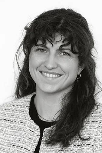 Woman with long wavy hair, smiling, wearing a textured jacket over a black top. Black and white photo.