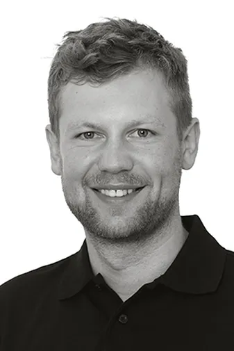 Smiling man with short hair wearing a dark polo shirt, posed against a plain white background.