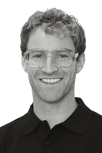 Smiling person wearing clear glasses and a black polo shirt, against a plain white background.