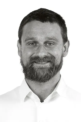 Man with a beard and short hair, wearing a white shirt, smiling against a plain white background.