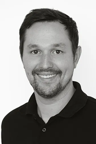 Man smiling in black and white portrait, wearing a dark polo shirt against a plain white background.
