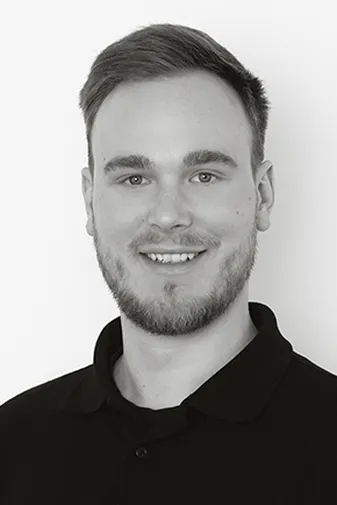 A man with short hair and a beard smiling, wearing a dark polo shirt, against a plain white background.