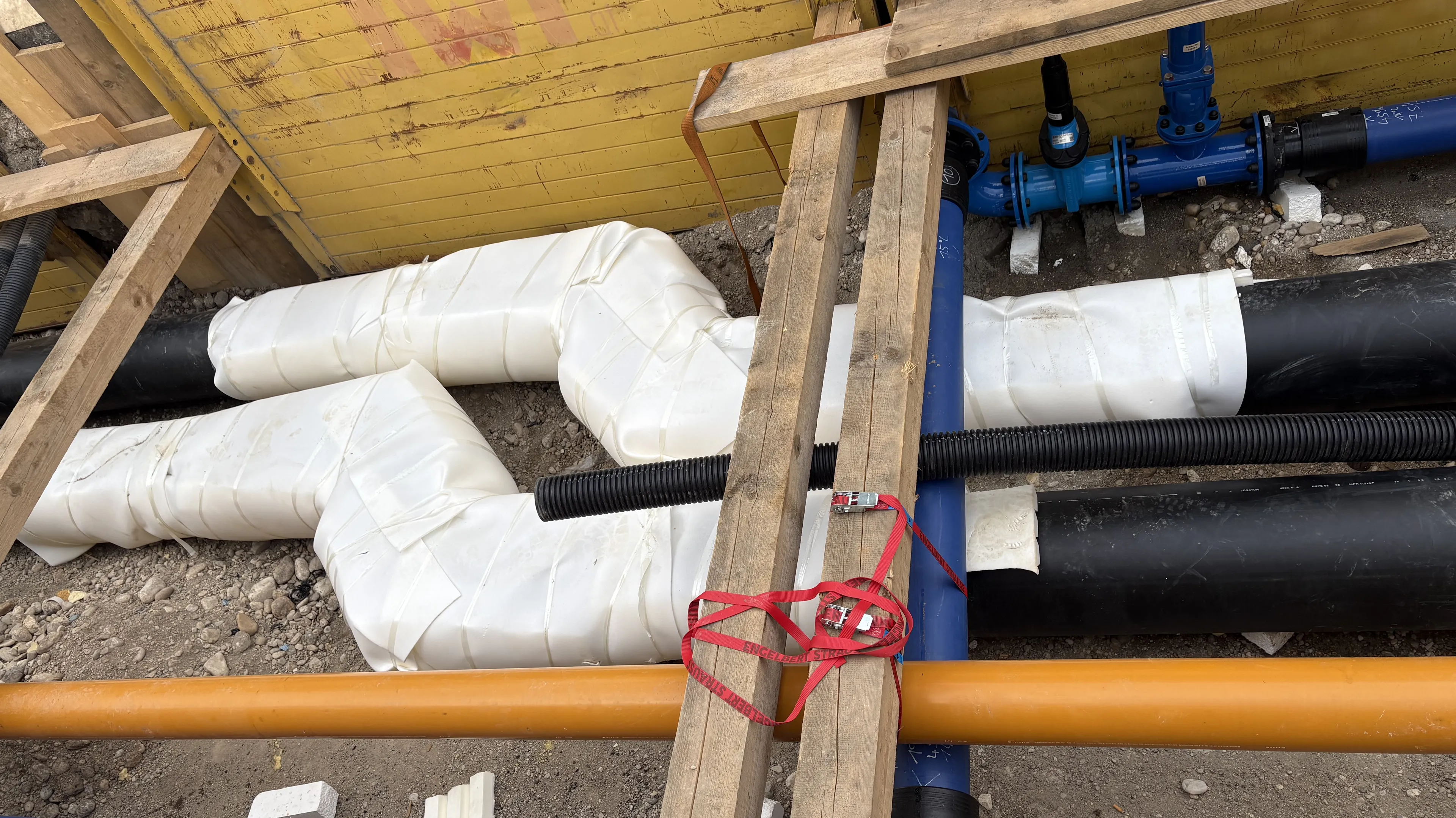 Baustellensituation mit verlegten Versorgungsleitungen, isolierten Rohrsystemen und technischen Anschlüssen für die Energie- und Gebäudetechnik. Die Installation dient der sicheren Verteilung von Wärme, Wasser oder anderen Medien innerhalb einer technischen Infrastruktur.