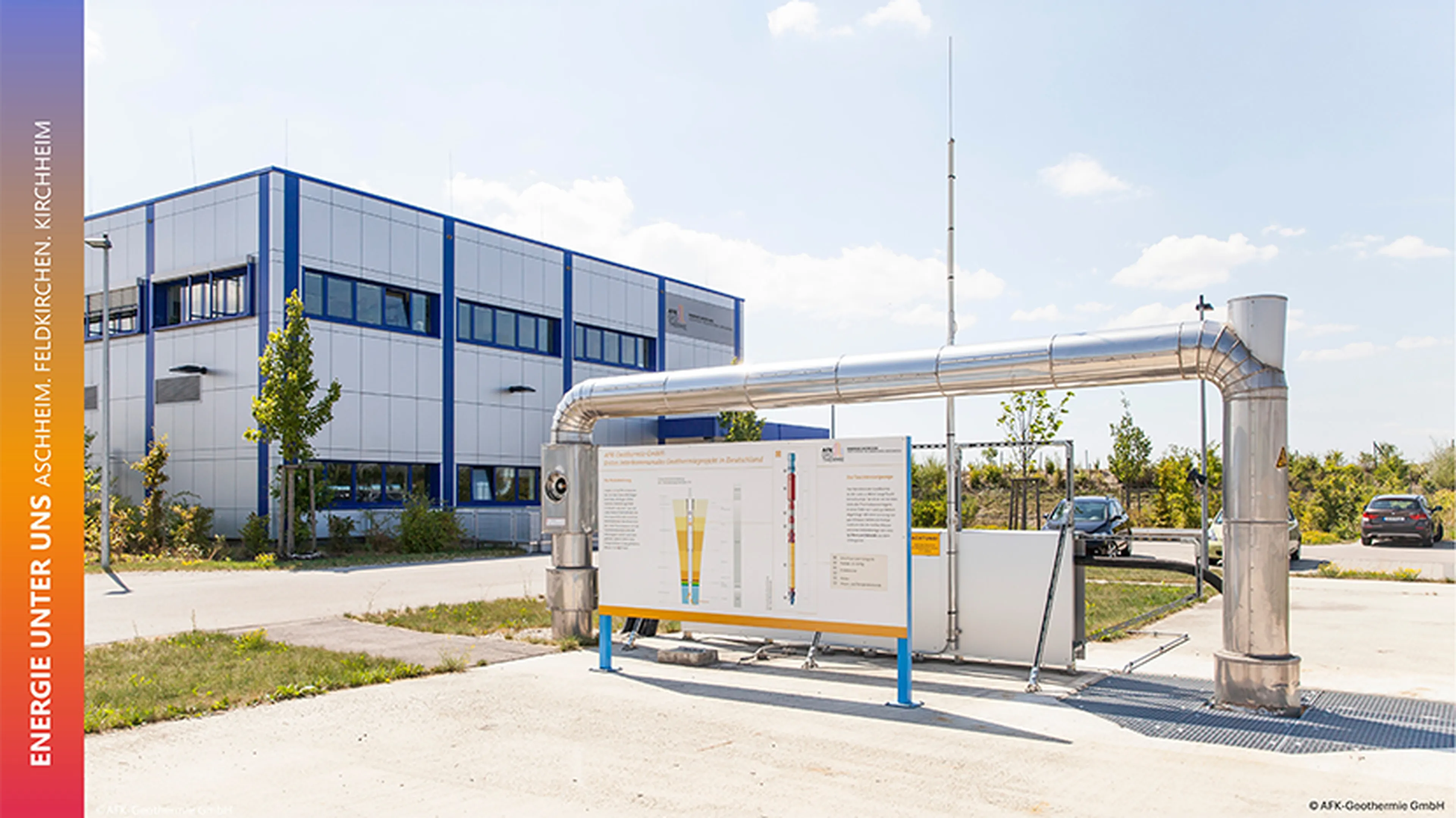 Industrial facility with piping and an informational display panel outside a modern building under a clear sky.