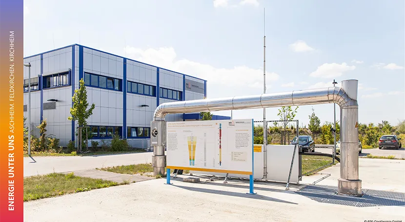 Industrial facility with piping and an informational display panel outside a modern building under a clear sky.
