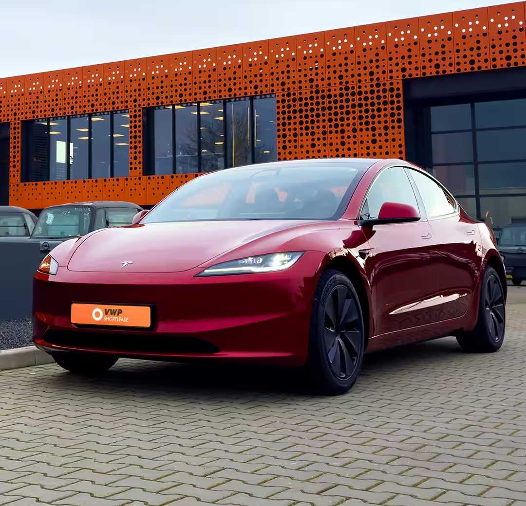Een rode Tesla is geparkeerd voor een gebouw met een oranje gevel. Op de voorkant van de auto staat het VWP Shortlease logo
