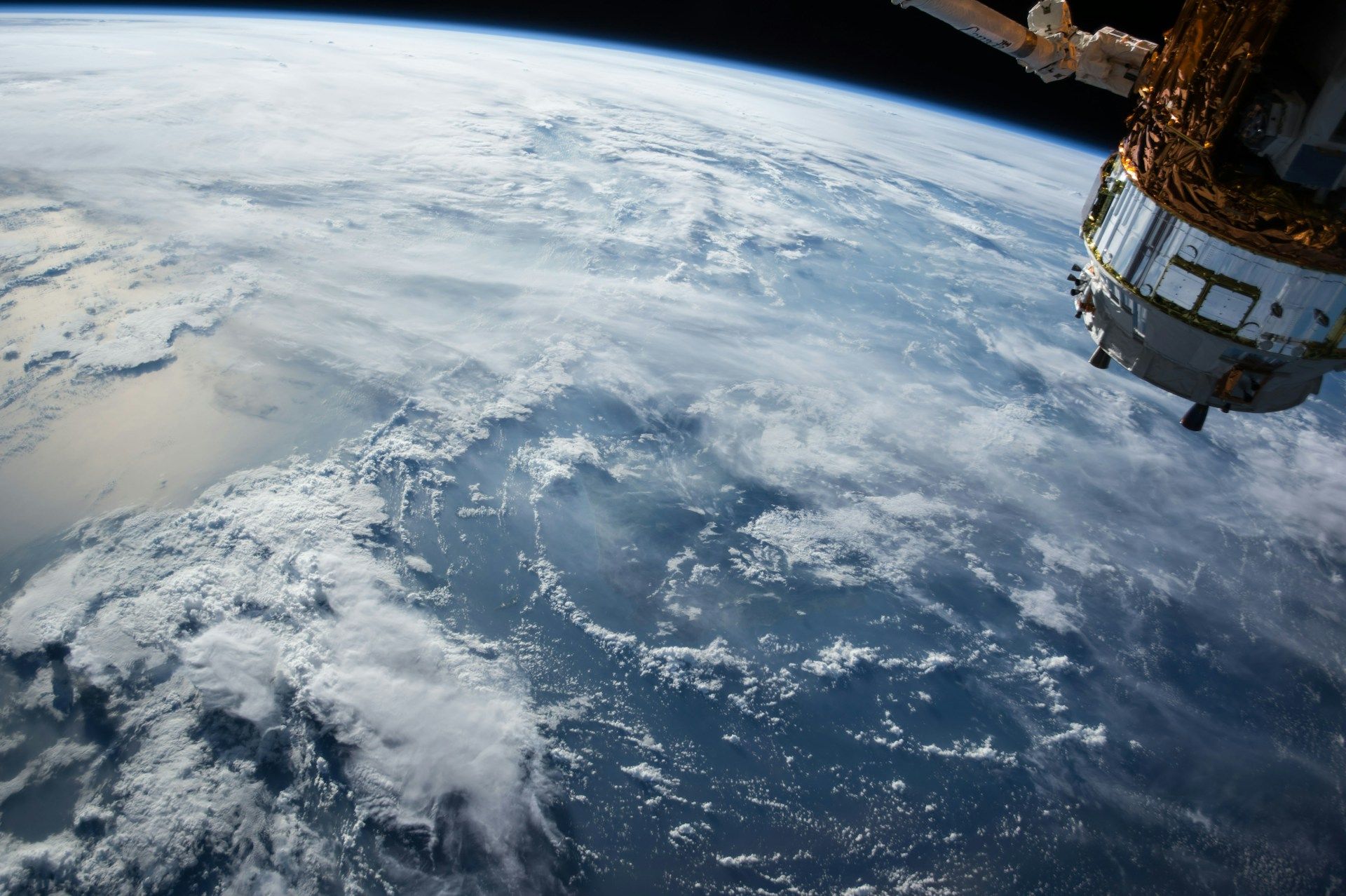 View of Earth from space, showing cloud formations over the ocean with a satellite partially visible on the right.