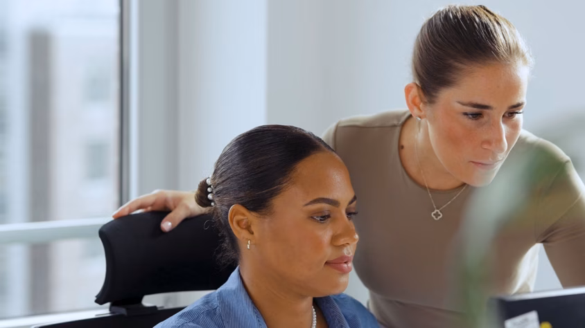 Zwei Mitarbeiterinnen arbeiten gemeinsam an einem Computerarbeitsplatz im Büro.