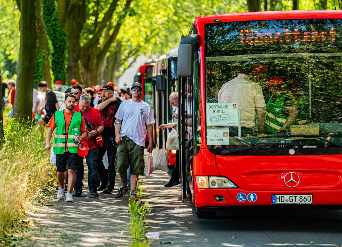 Menschen steigen an einer Haltestelle aus mehreren roten Shuttlebussen aus.