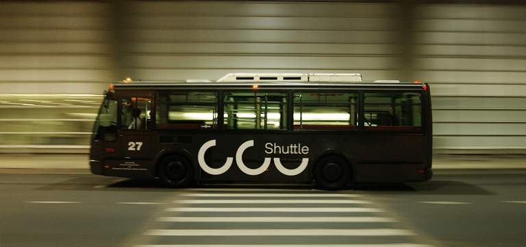 Dunkler Bus mit Shuttle-Beschriftung fährt mit Bewegungsunschärfe durch eine Unterführung.
