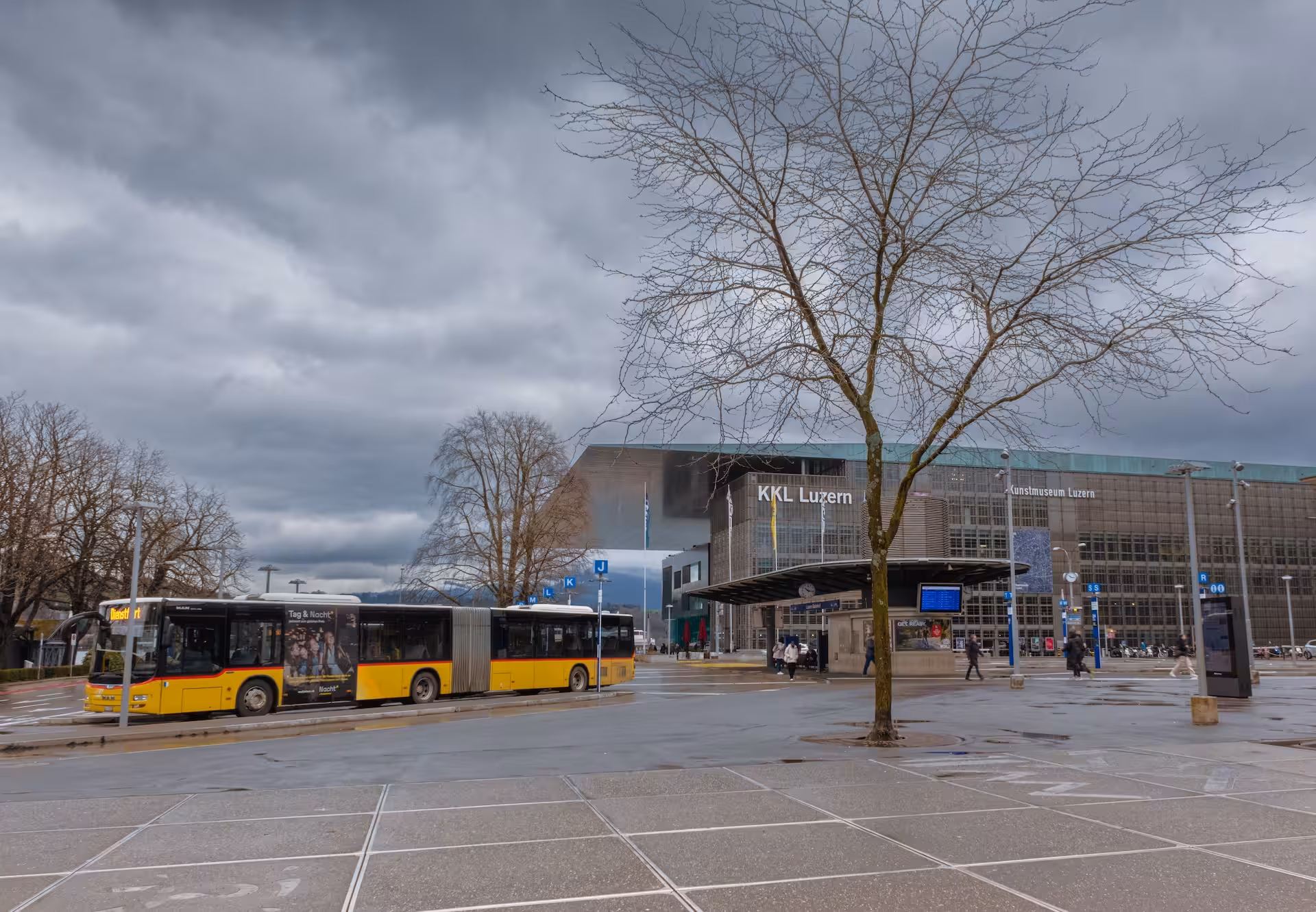 Gelber Gelenkbus an einer Haltestelle vor dem Kultur- und Kongresszentrum KKL Luzern bei bewölktem Himmel.