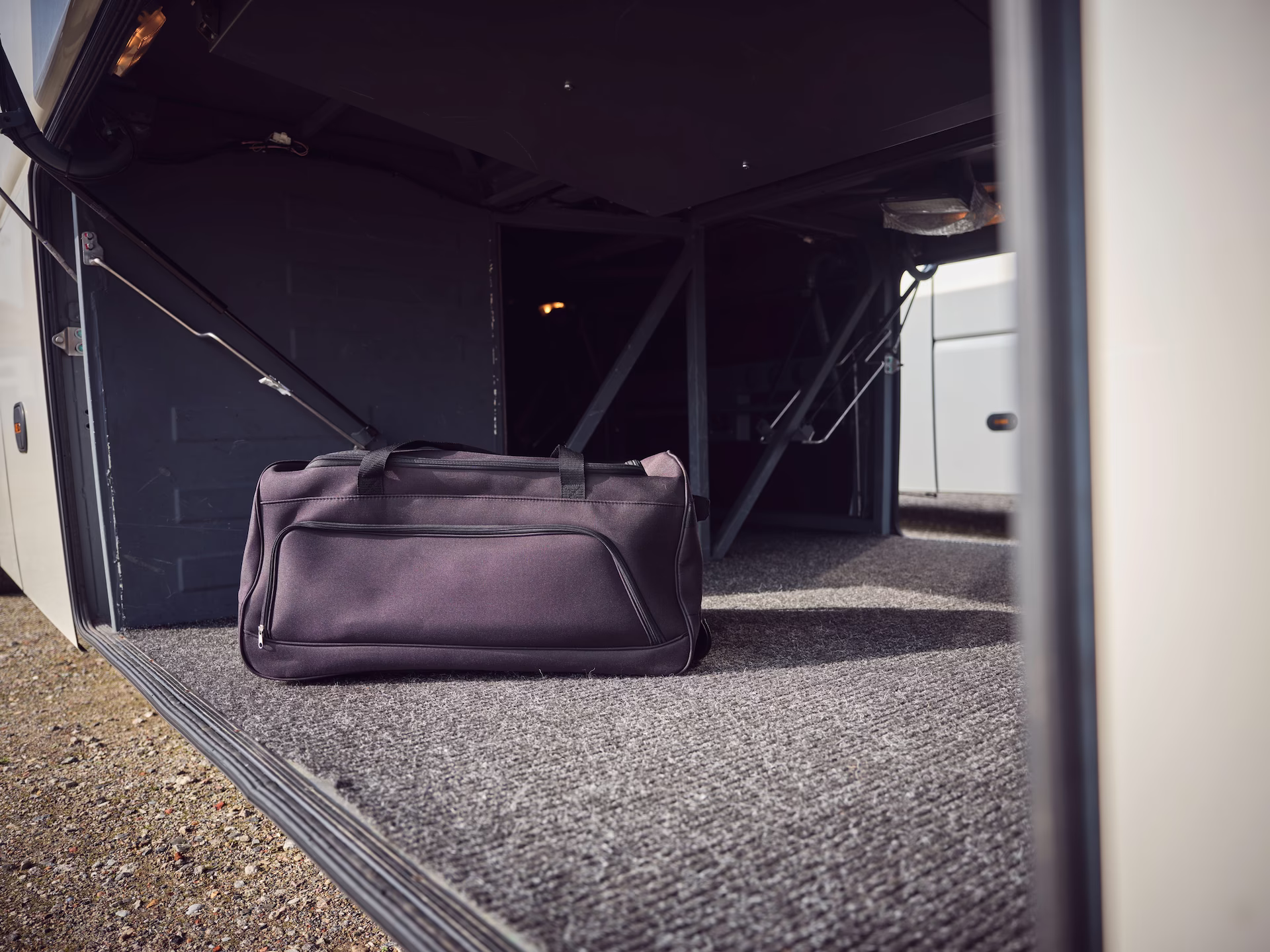 Nahaufnahme einer großen, dunklen Reisetasche, die im teppichausgelegten, geöffneten Kofferraum eines Reisebusses steht.