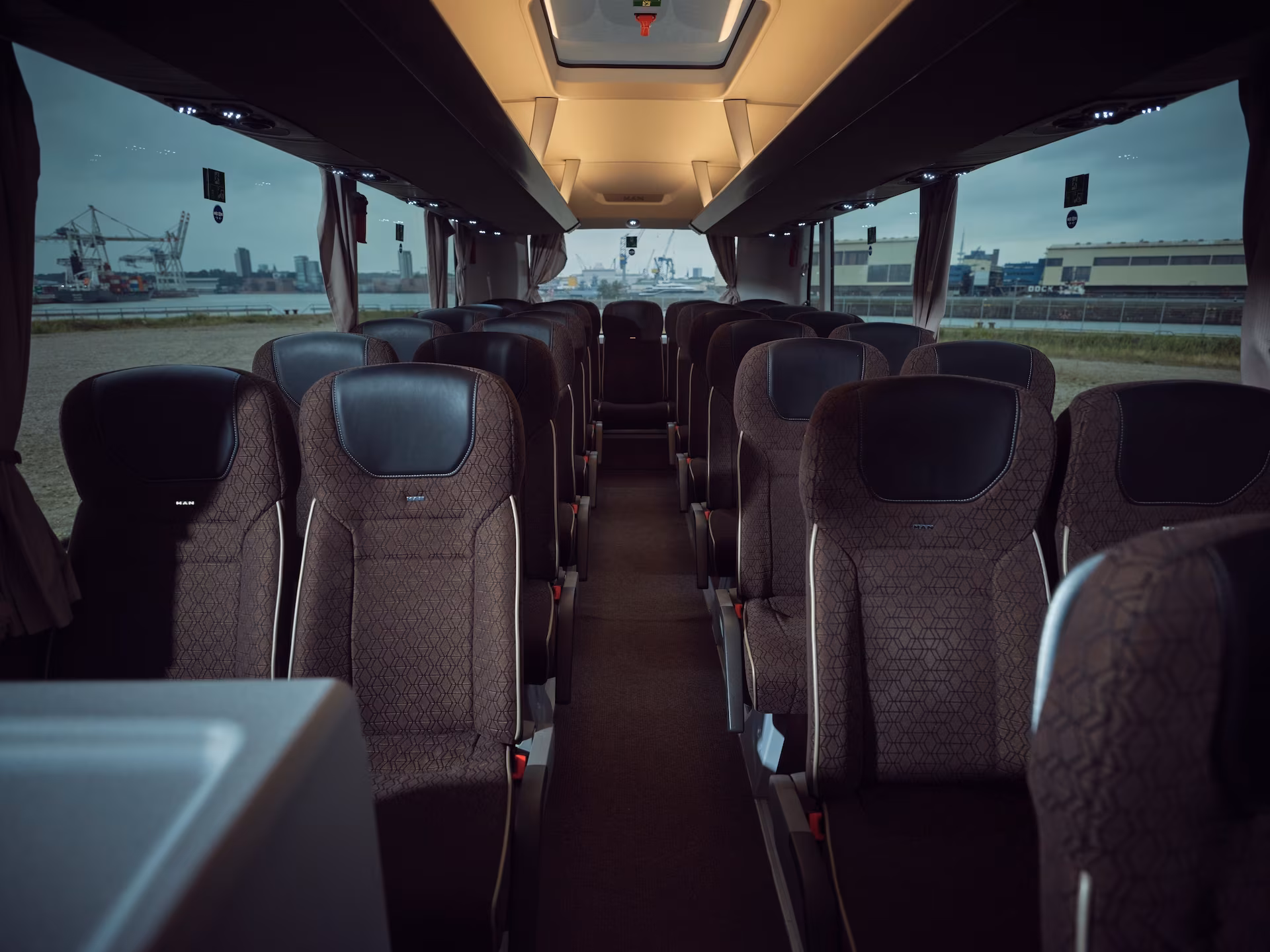 Blick von vorne durch den Reisebus-Mittelgang nach hinten auf die Sitzreihen und die Rückbank vor einer Hafenkulisse.