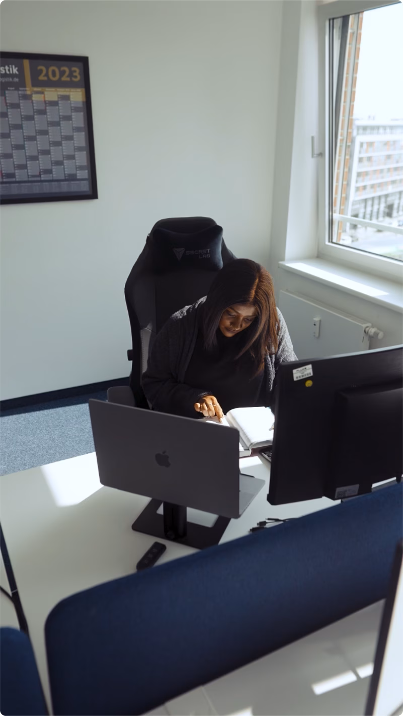 Mitarbeiterin arbeitet konzentriert an ihrem Schreibtisch und prüft Unterlagen am Computerarbeitsplatz.