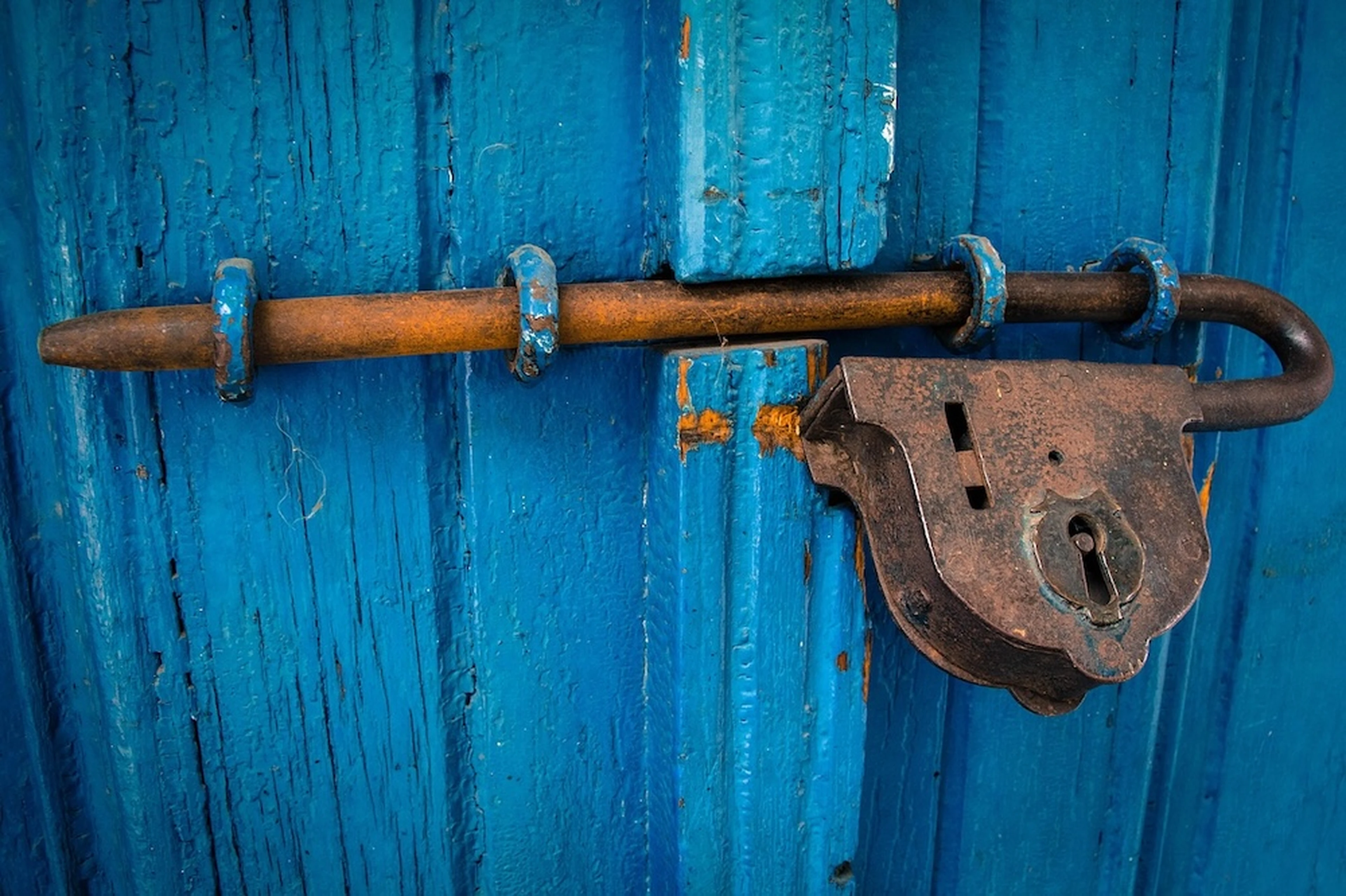 Rusty lock and latch on a weathered blue wooden door, showing signs of age and wear.