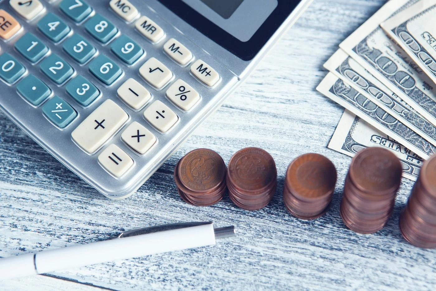 Calculator, pen, stacked coins, and dollar bills on a table