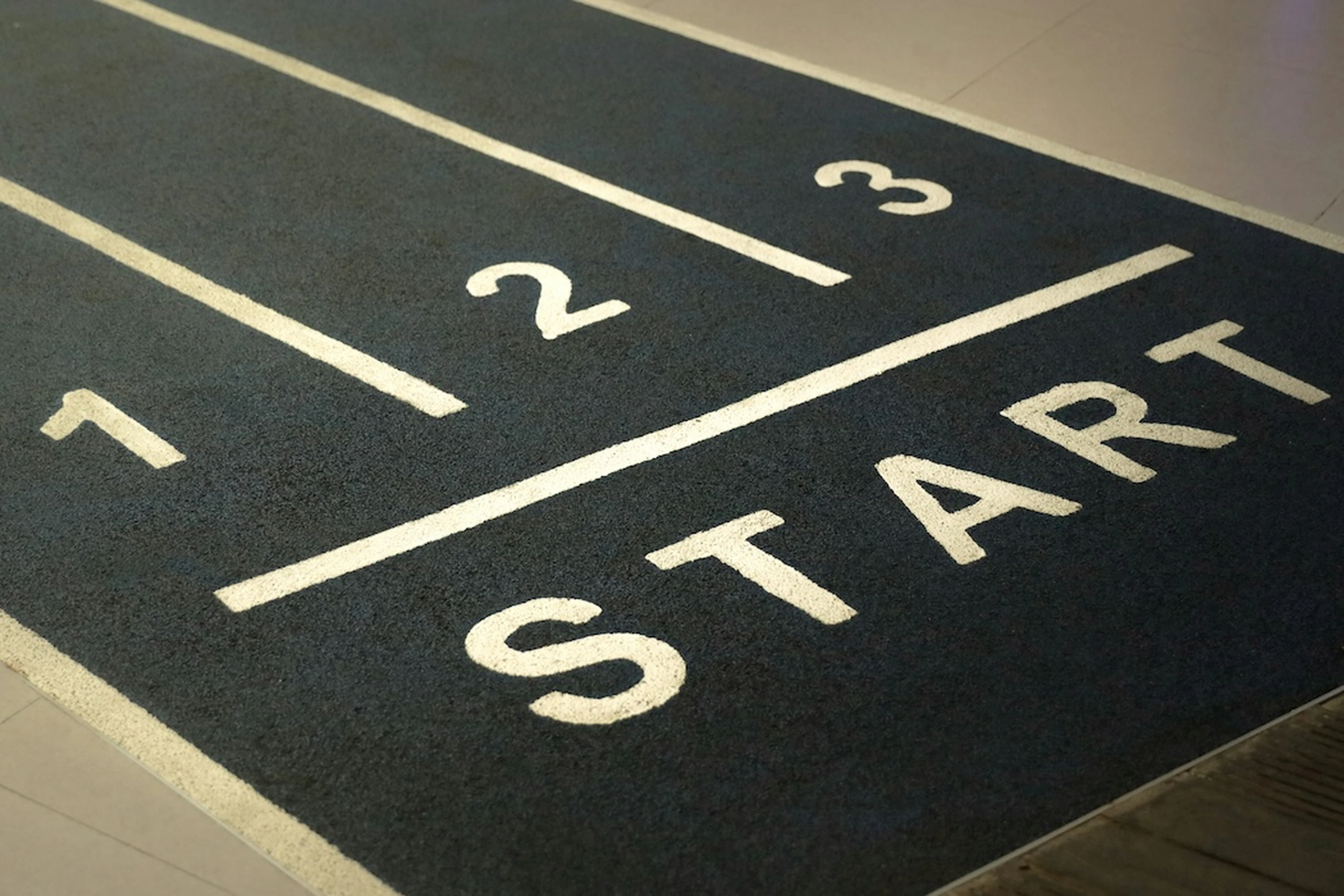 Close-up of a starting line with lanes numbered 1, 2, 3 and the word START on a dark track surface.
