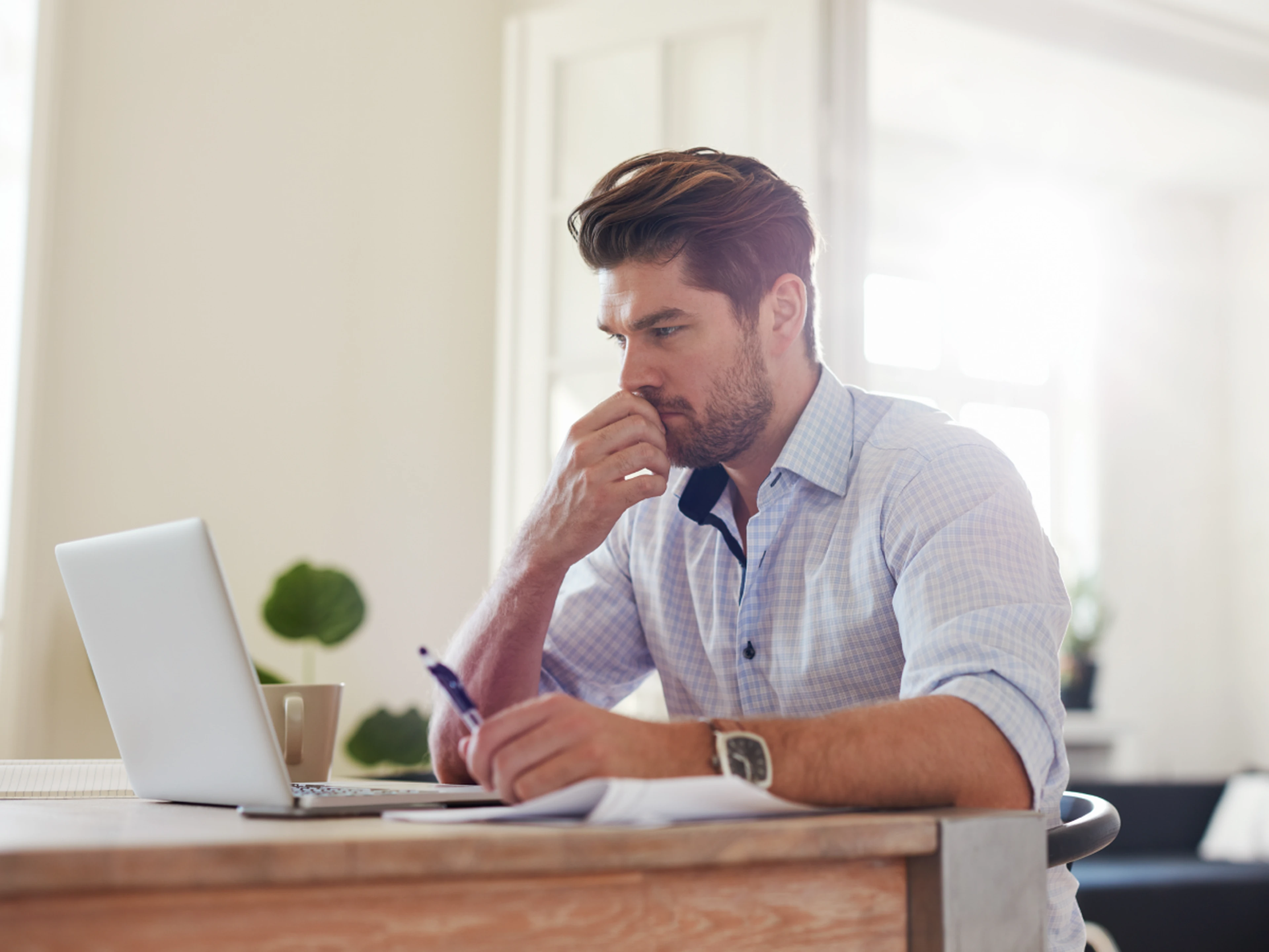 Thinking man sitting at desk with laptop and paper