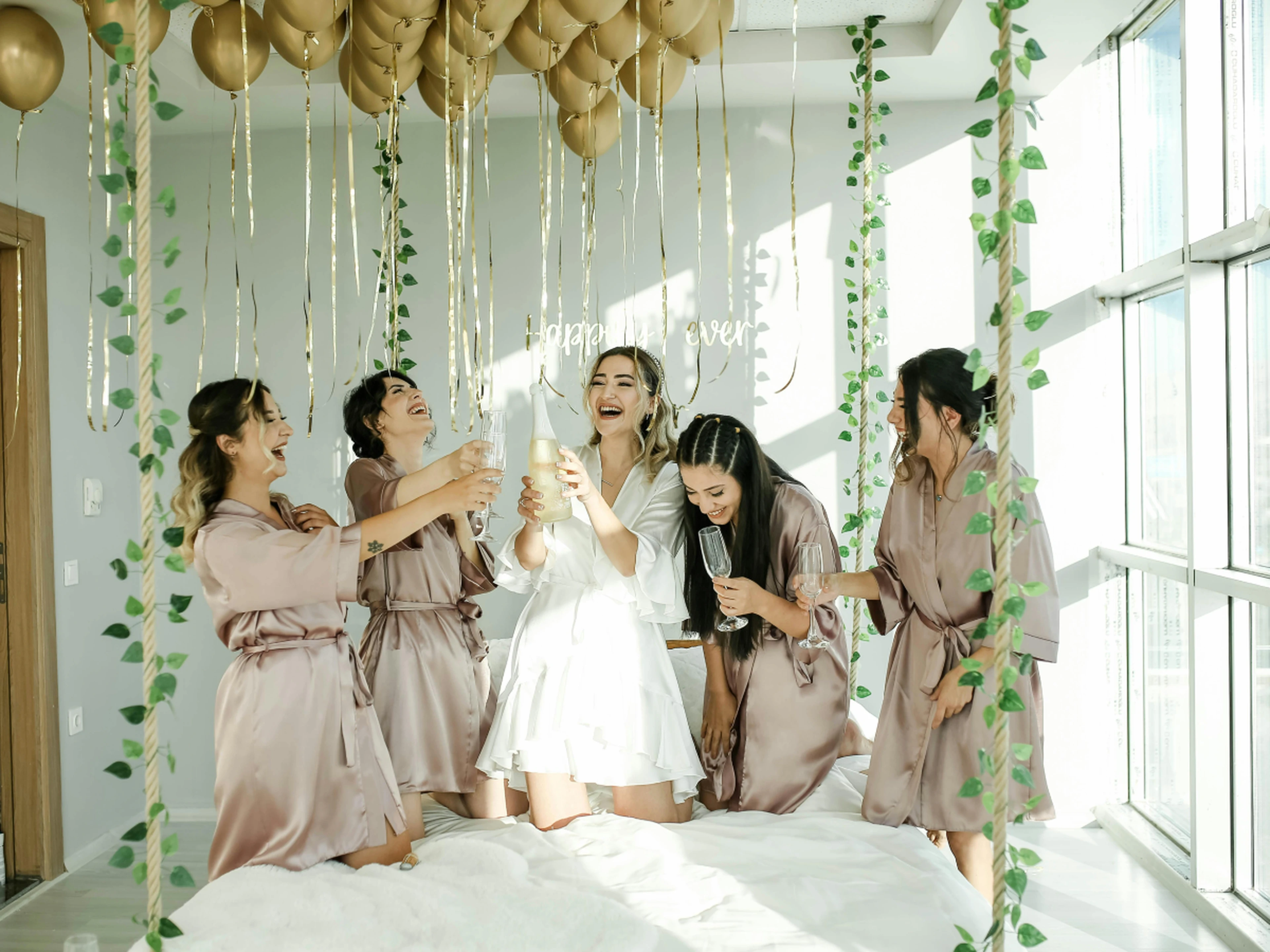 group of bridesmaids celebrating in hotel room with prosecco
