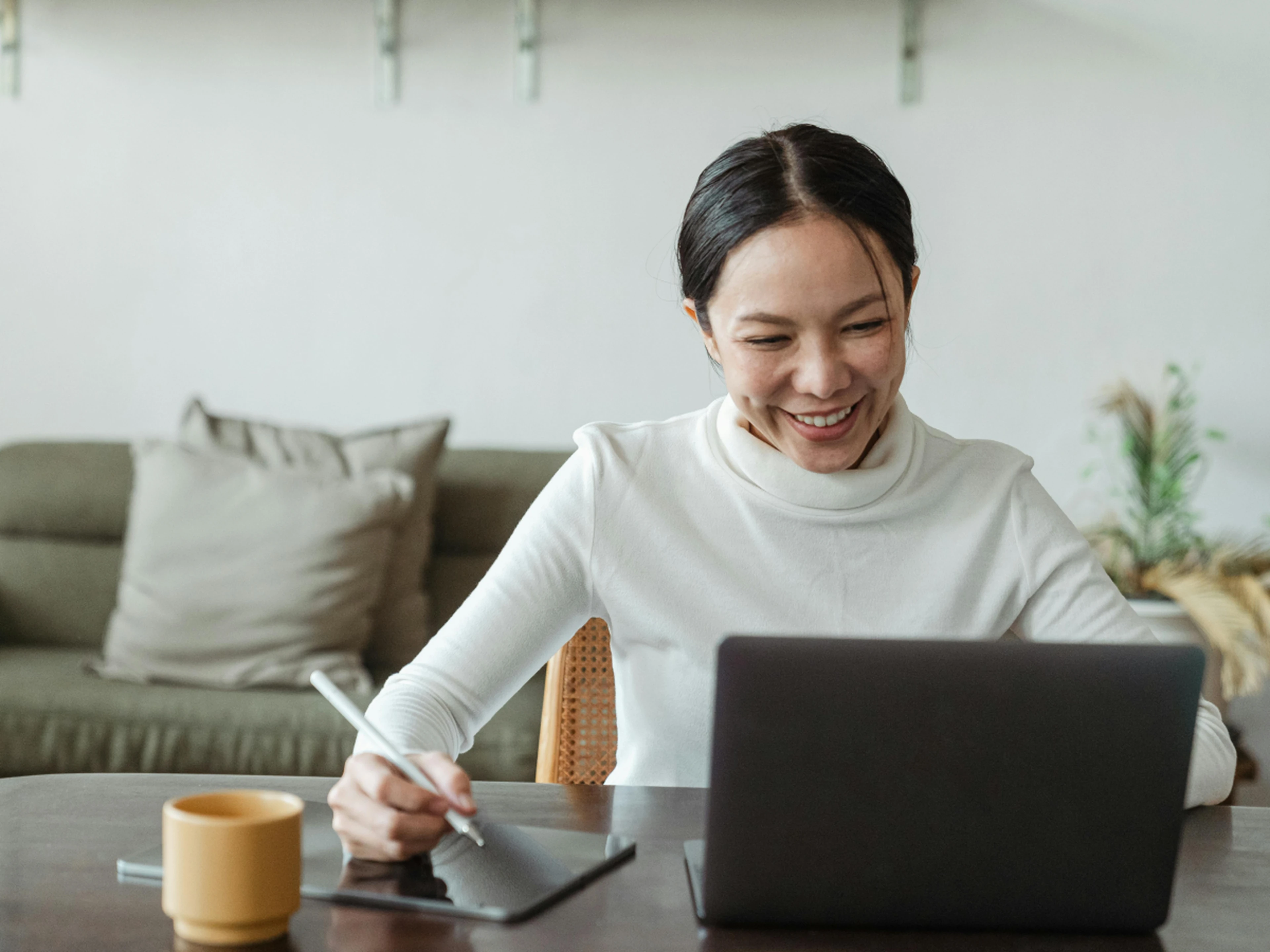 Woman at desk looking at laptop and writing on a tablet