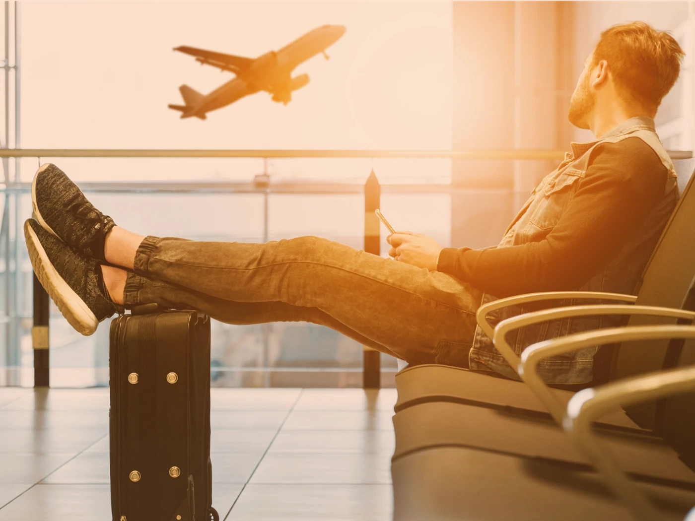 traveler waiting at the airport with his suitcase, watching an airplane take off