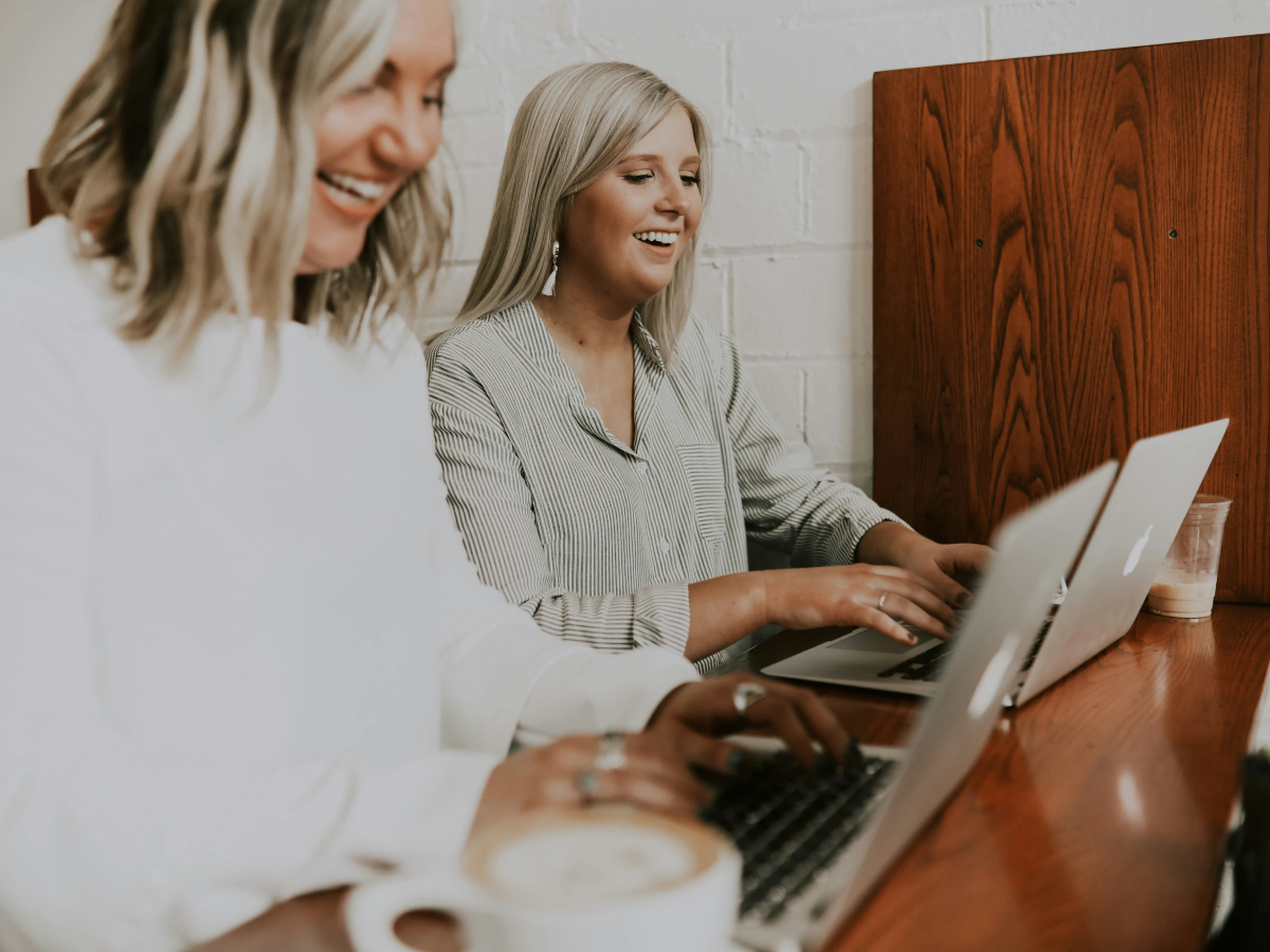 Two women smiling and working on laptops at a hotel reception desk