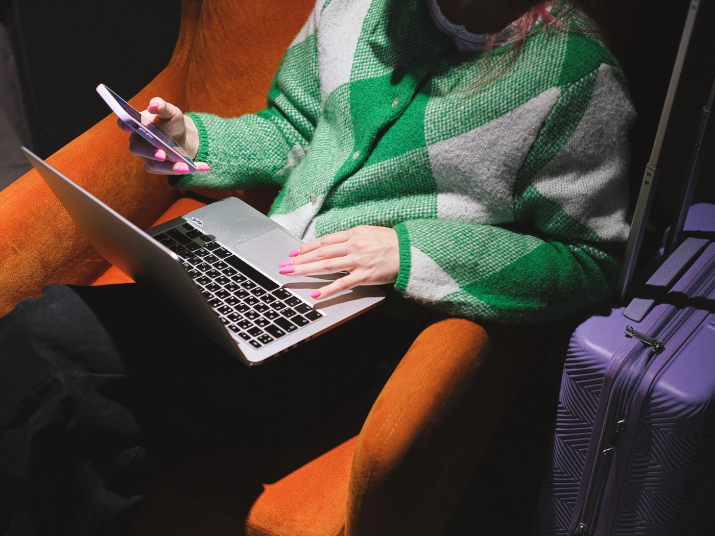 traveler with a suitcase looking simultaneously on a laptop and smartphone