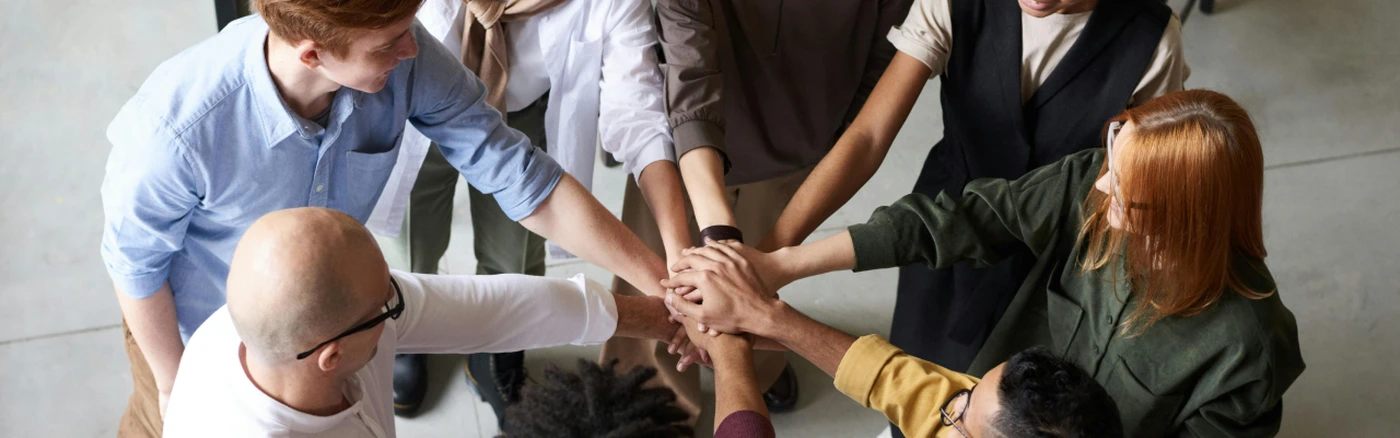 A team of hotel staff standing in a circle, stacking their hands together in a gesture of teamwork