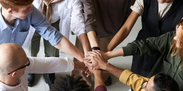 A team of hotel staff standing in a circle, stacking their hands together in a gesture of teamwork