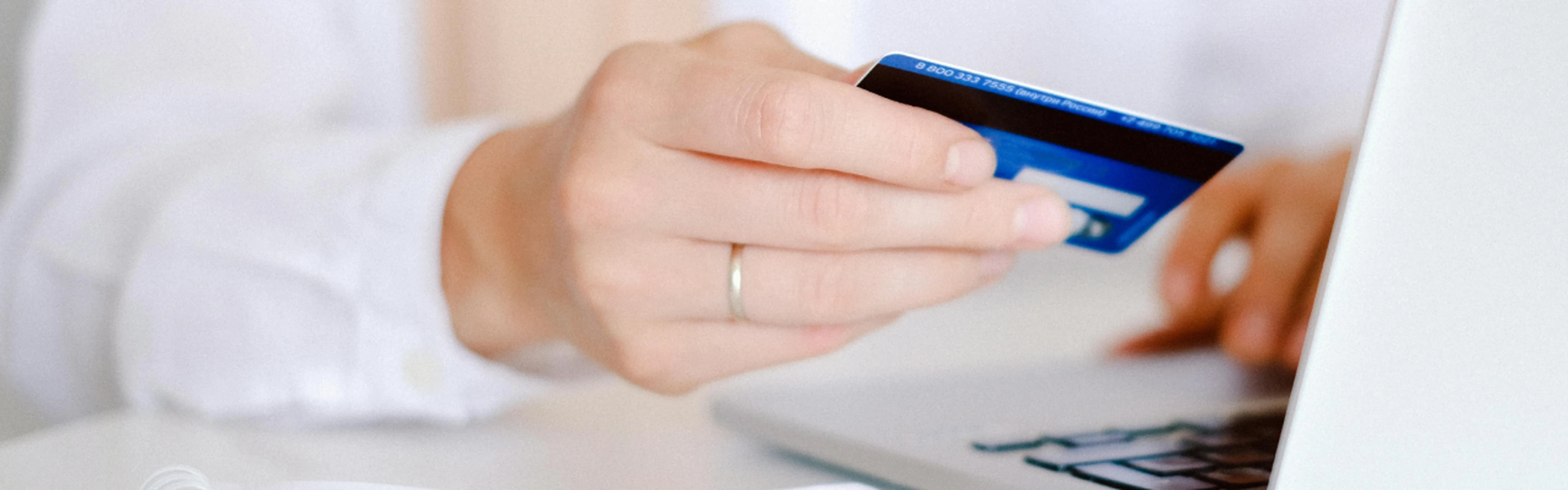 person holding a blue credit card while using a laptop, performing an online payment
